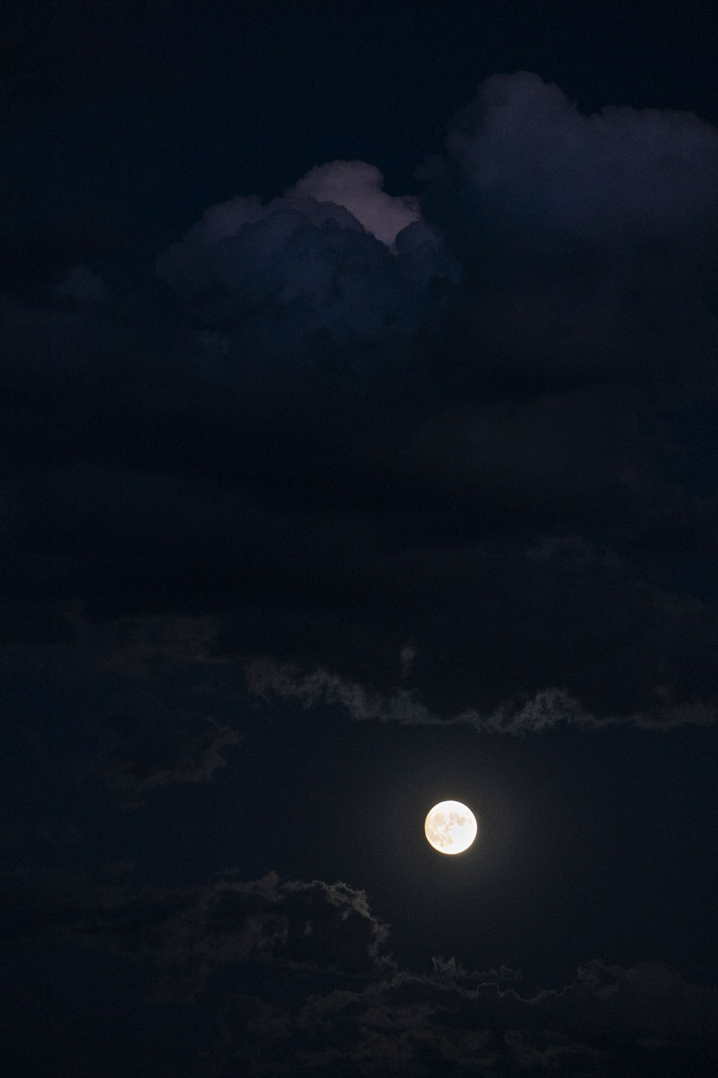 The bright full moon in the twilight sky underneath a big lit cloud